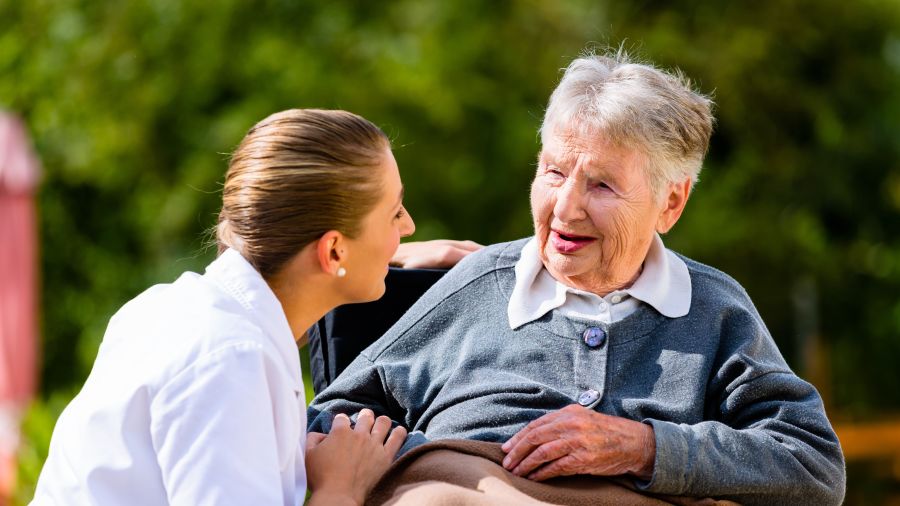 Nurse holding hands with senior woman in wheelchair